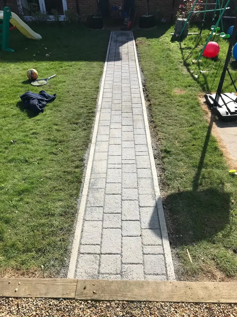 A block paved path with a timber sleeper edge running through a lawn