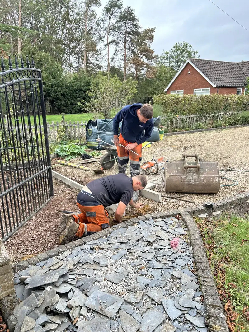 Two groundworkers laying edging and a slate border beside new gates