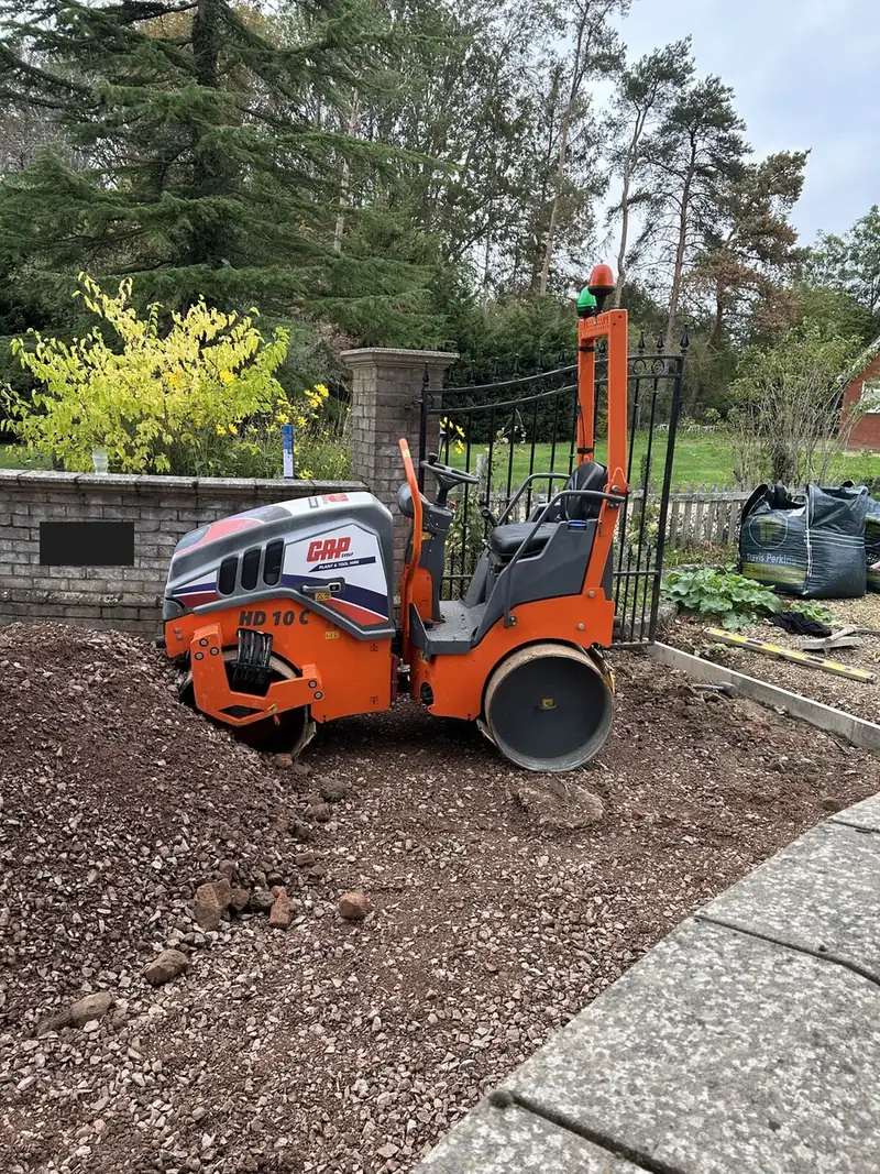 Twin drum roller compacting stone sub-base beside a brick wall