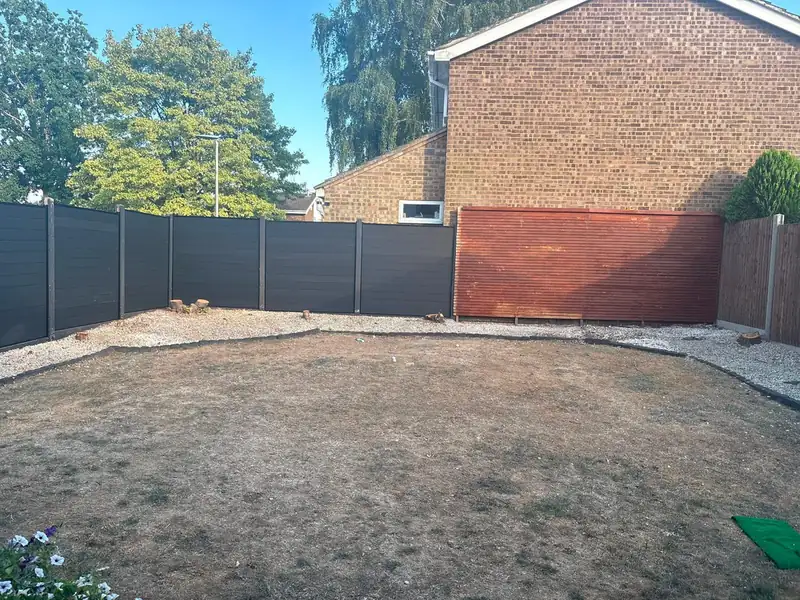 A dry back lawn before groundworks, with a dark fence and a brick house behind