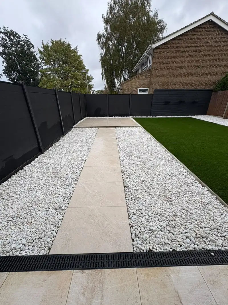 Porcelain path through white gravel and a lawn, with a black drain channel across the front