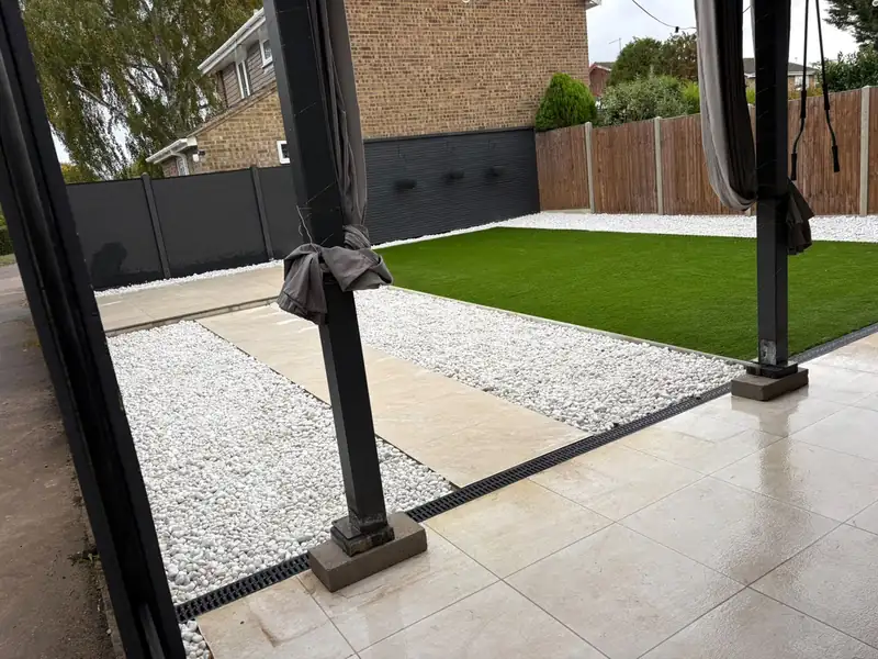 Porcelain paving, white gravel and a lawn with a black drainage channel along the edge