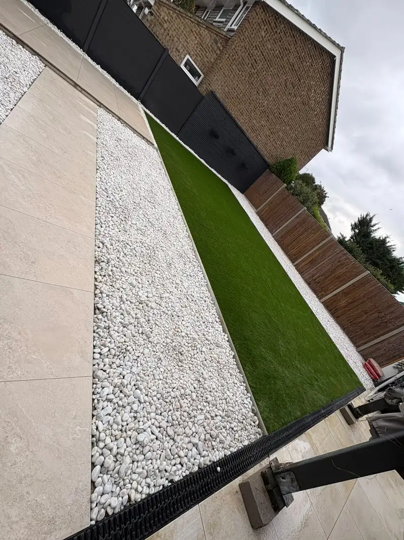 Porcelain stepping slabs through white gravel beside a lawn and a dark fence