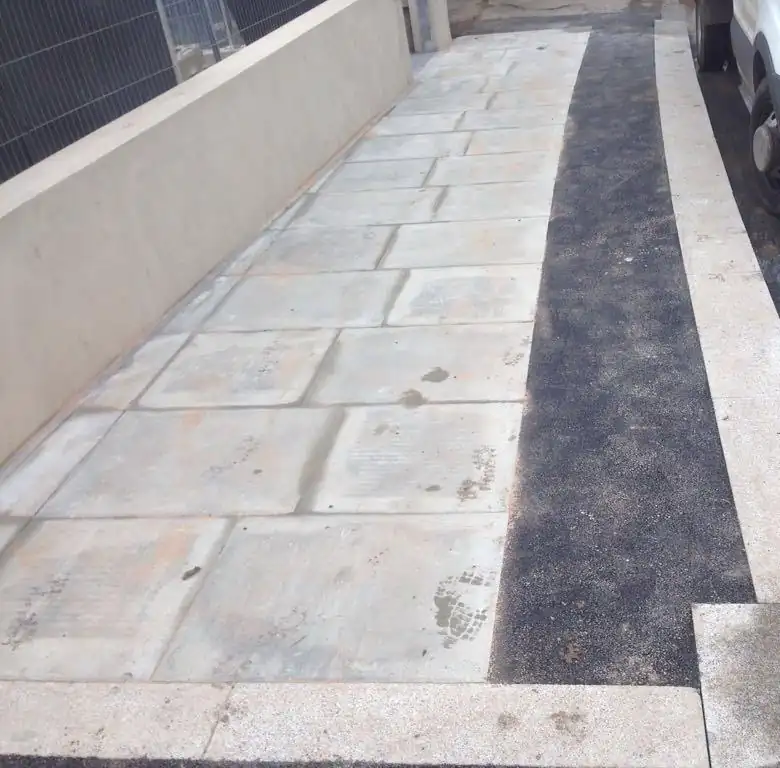 A sandstone paved path next to a tarmac strip and a granite kerb