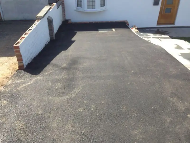 A fresh tarmac drive beside a white rendered wall and a house