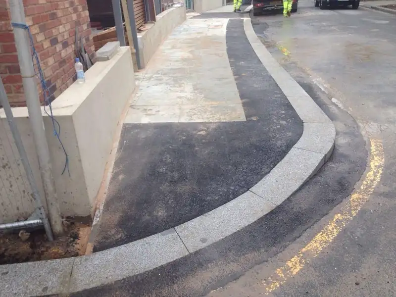 A tarmac drive curving around a granite kerb beside a rendered wall