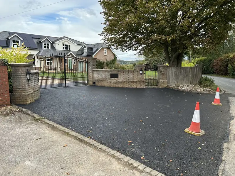 Finished tarmac driveway leading to a brick wall and black metal gates
